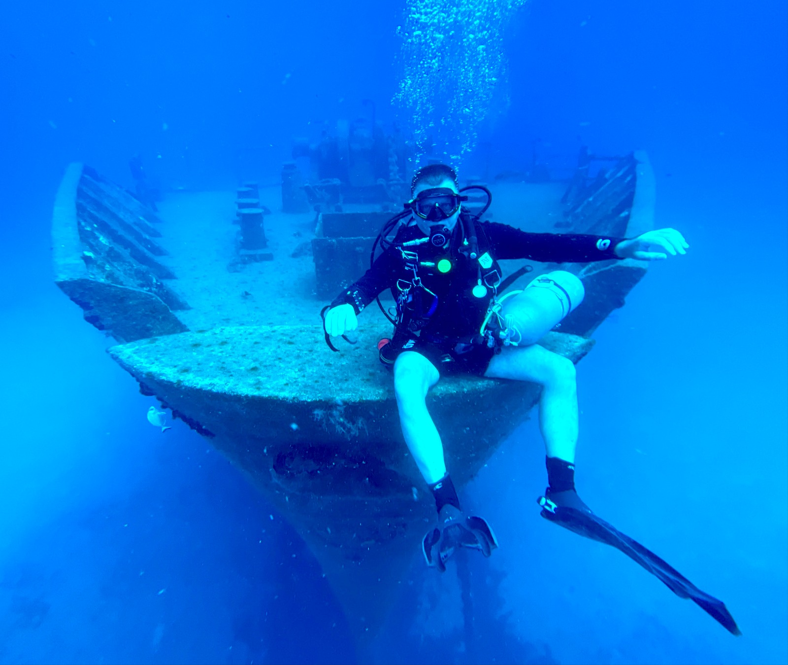 Diver sitting on the bow of a large wreck in clear blue water off Malta